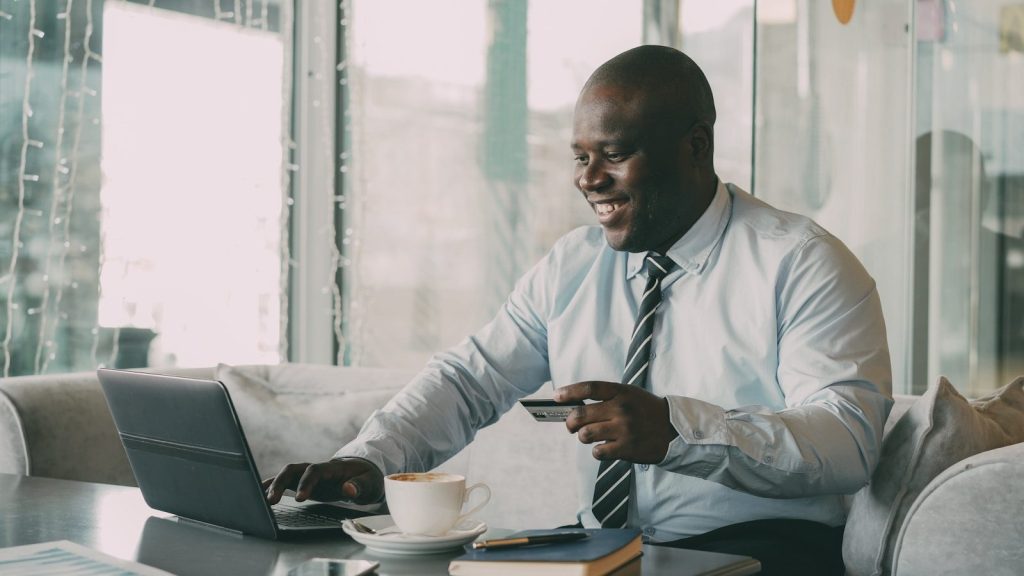 Man with credit card using laptop with coffee.